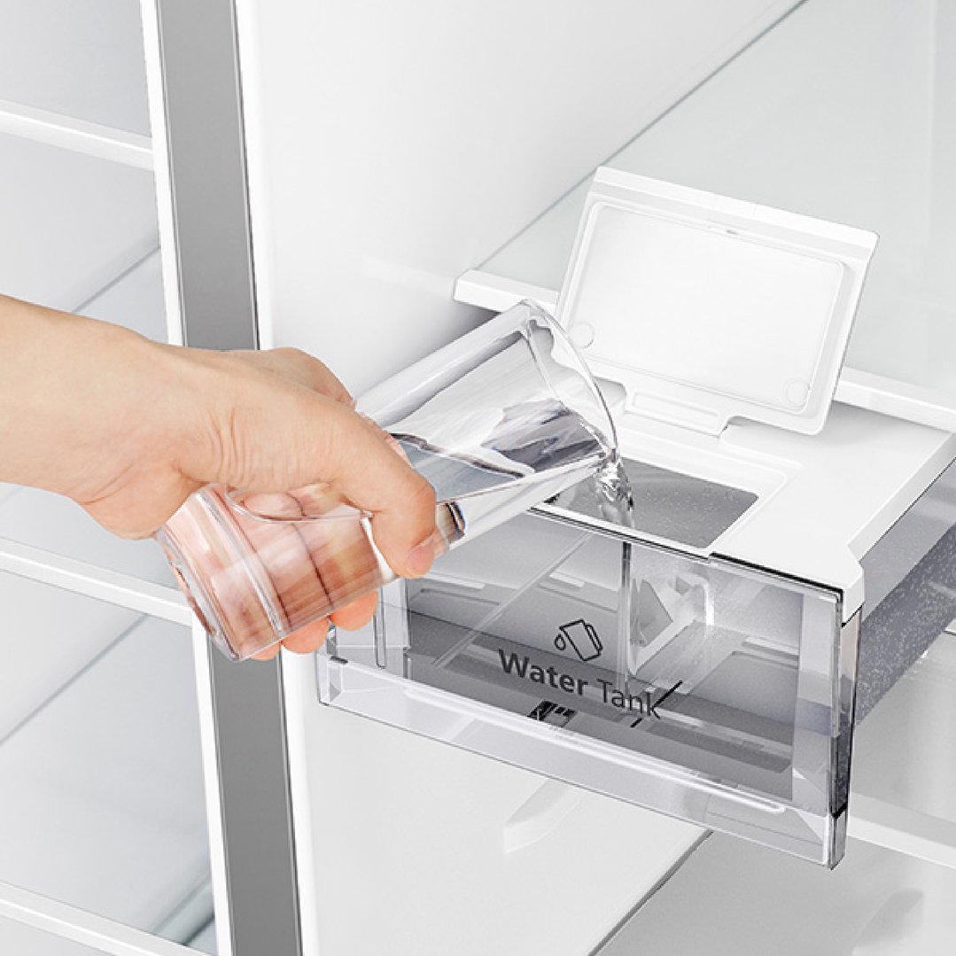 Hand pouring water from a glass into the water tank of a fridge