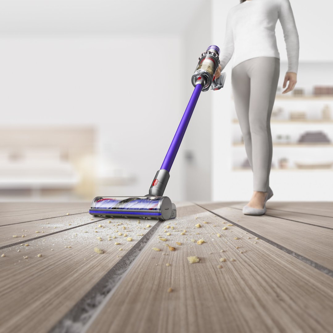 Woman vacuuming crumbs and dust from a wooden floor with a Dyson V11 Stick Vacuum