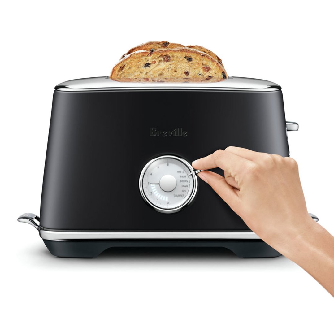 Hand adjusting the settings on a black Breville toaster with toast inside
