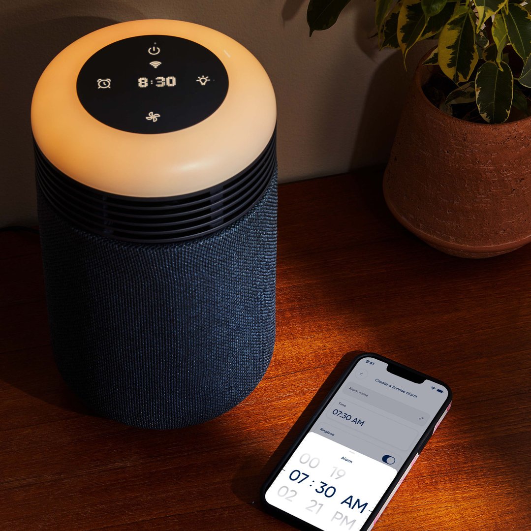 Blue air purifier on a wooden surface with a phone and plant