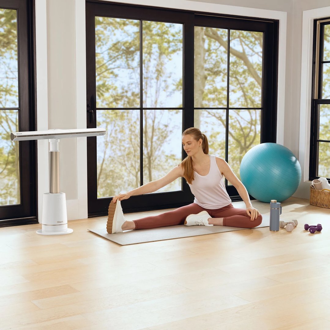 Woman stretching on a yoga mat with a Shark TurboBlade fan nearby