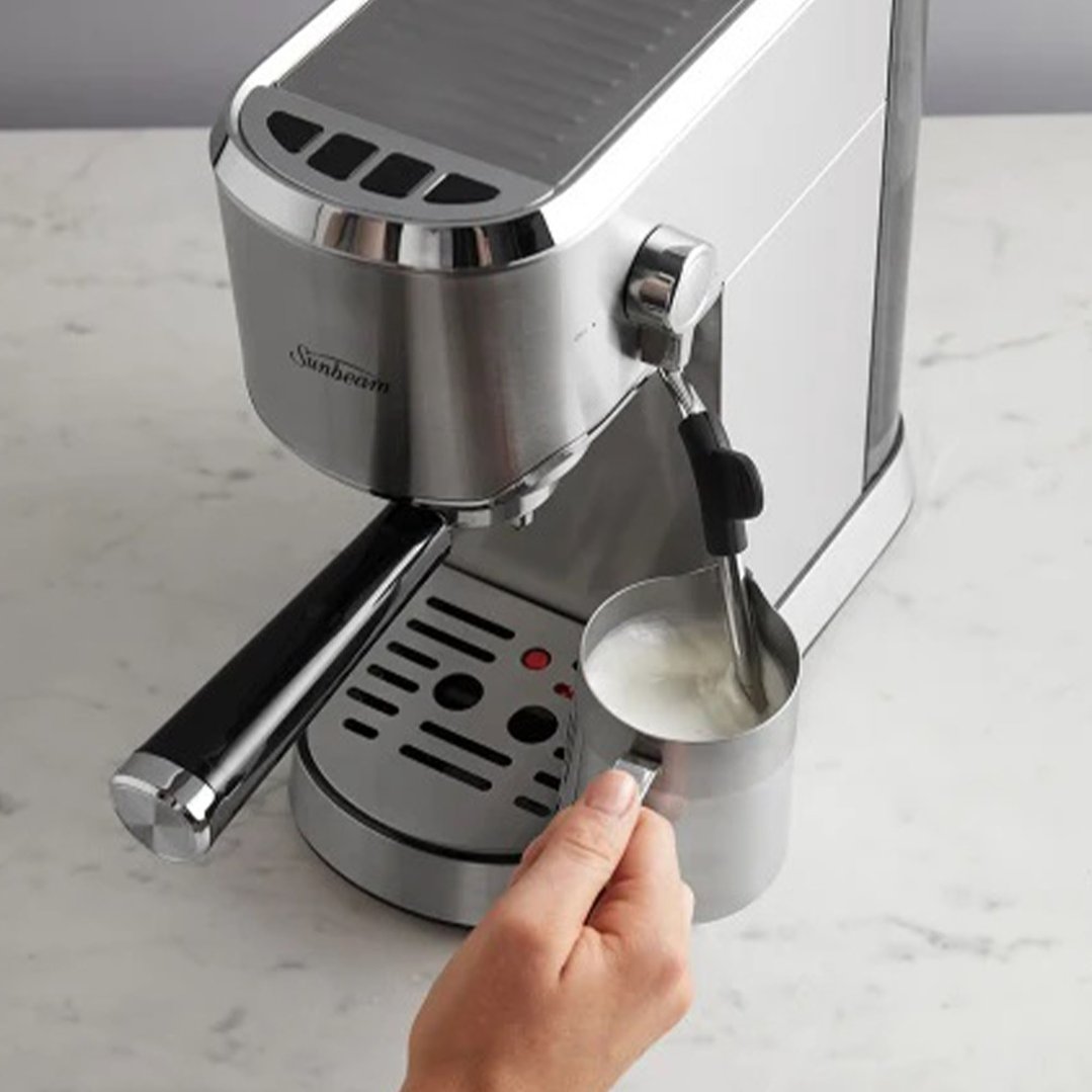 Hand holding a milk jug under the steam wand of a Sunbeam espresso machine