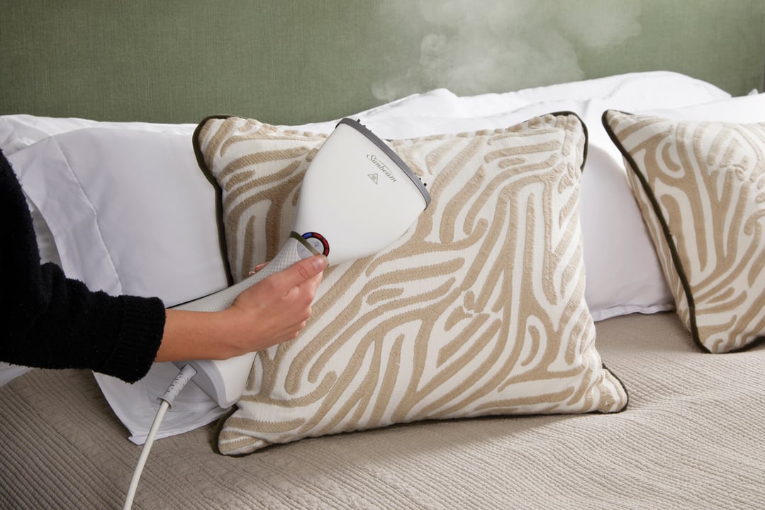 Handheld garment steamer steaming a decorative pillow on a bed