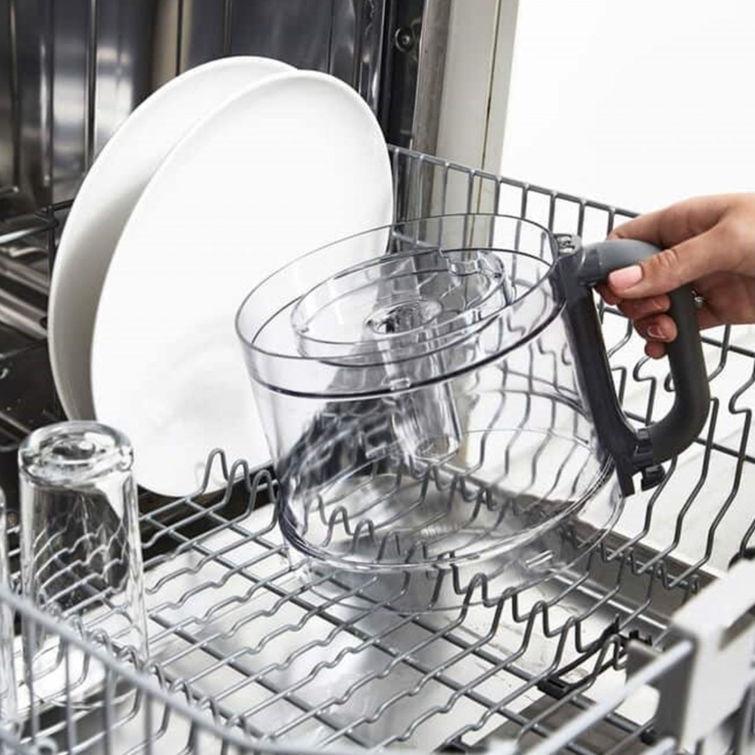 Hand placing a food processor bowl into a dishwasher with other dishes