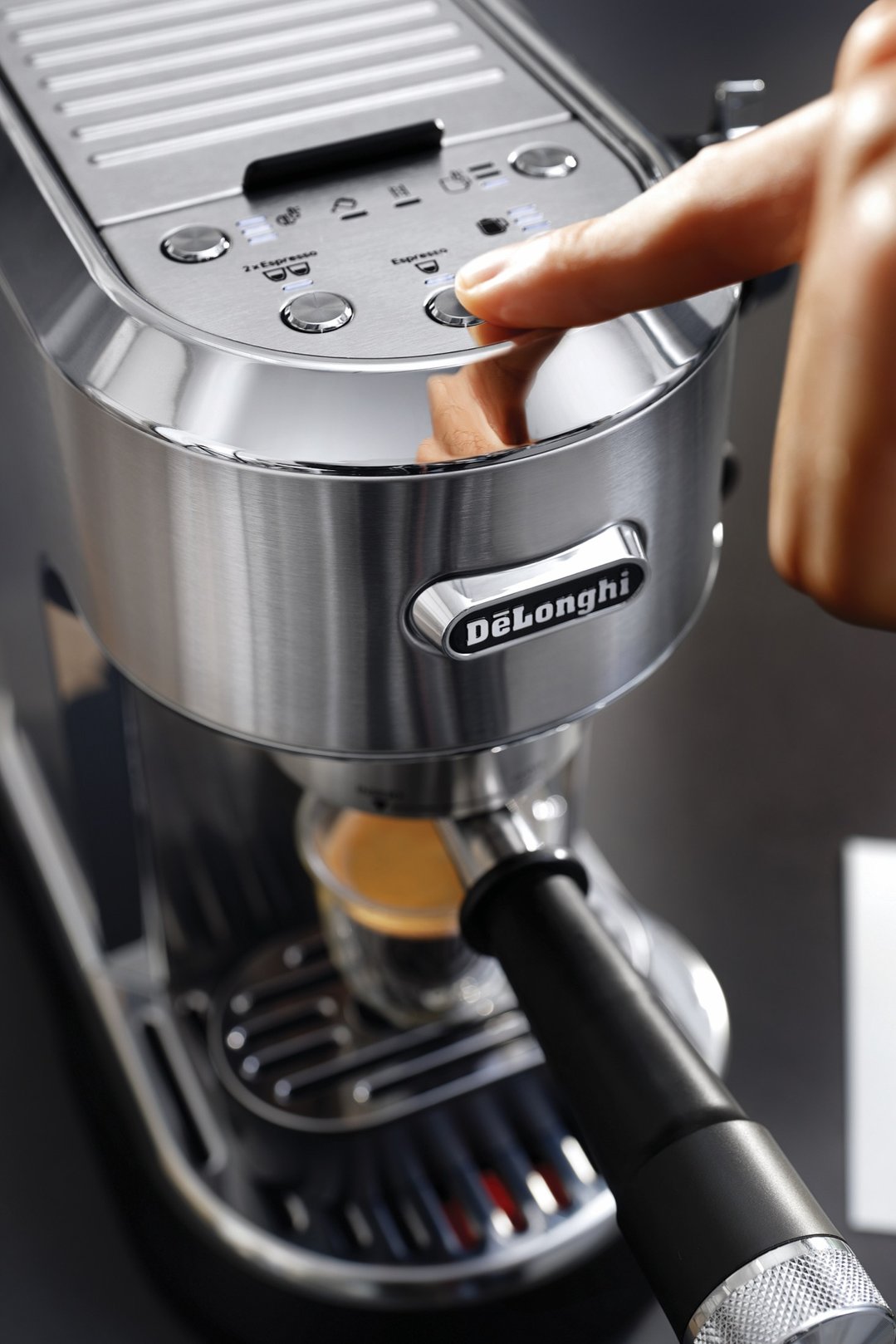 Hand pressing the espresso button on a DeLonghi coffee machine, making coffee