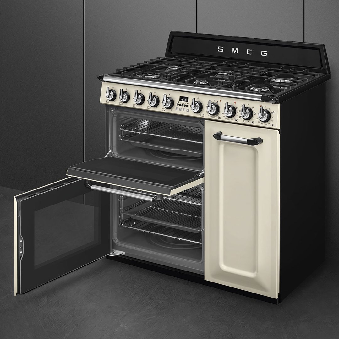 Cream freestanding cooker with open oven doors in a dark kitchen setting