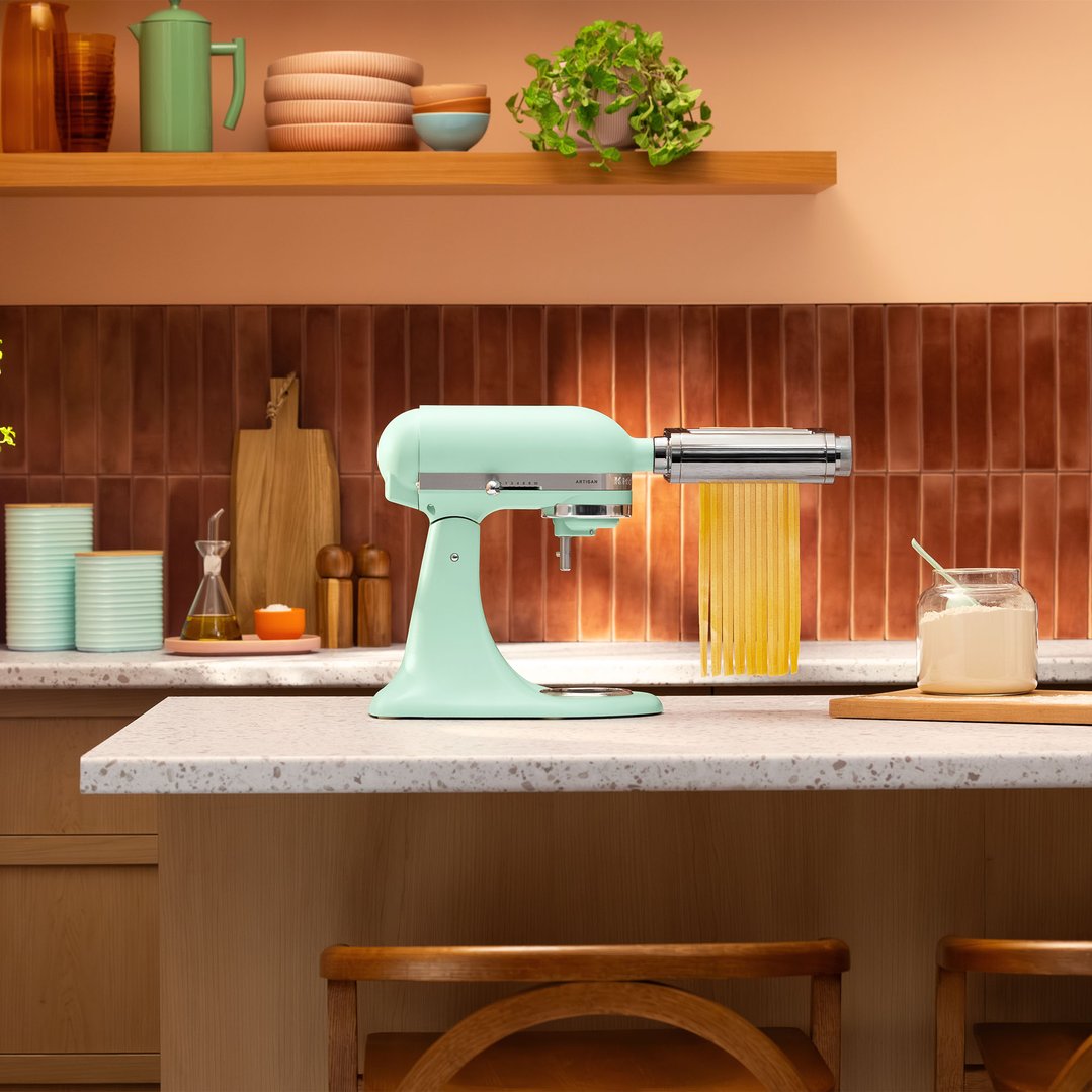 Spearmint KitchenAid Artisan Stand Mixer with pasta attachment making pasta in a kitchen