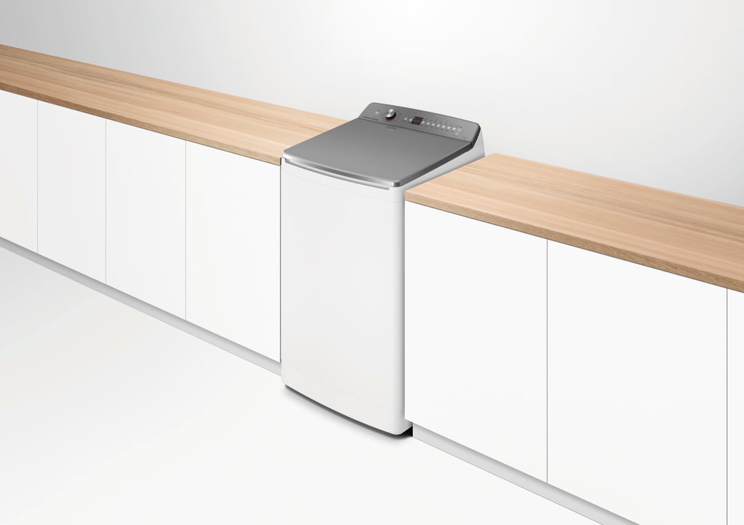 Top loader washing machine integrated into a wooden countertop in a white room