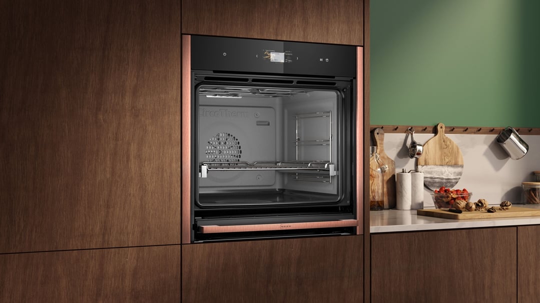Built-in oven with copper trim in a modern kitchen with green wall and wooden cabinets