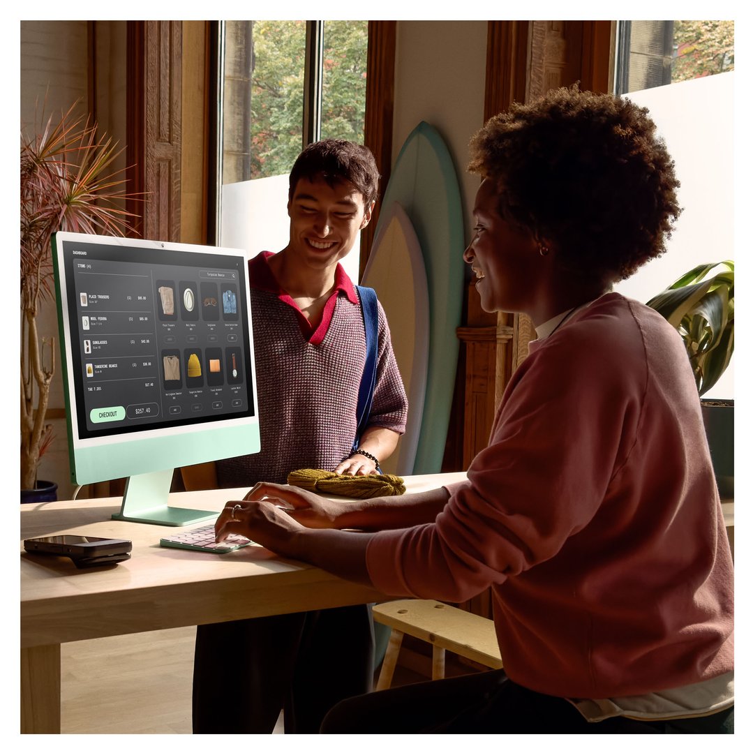 Two people interacting with an Apple iMac on a wooden desk