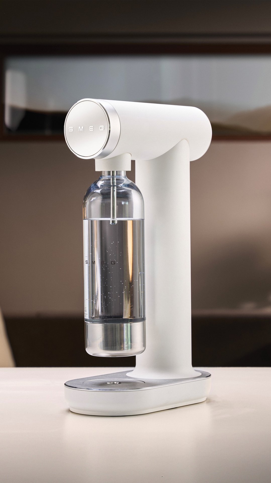 White soda maker with a clear bottle of water on a light surface