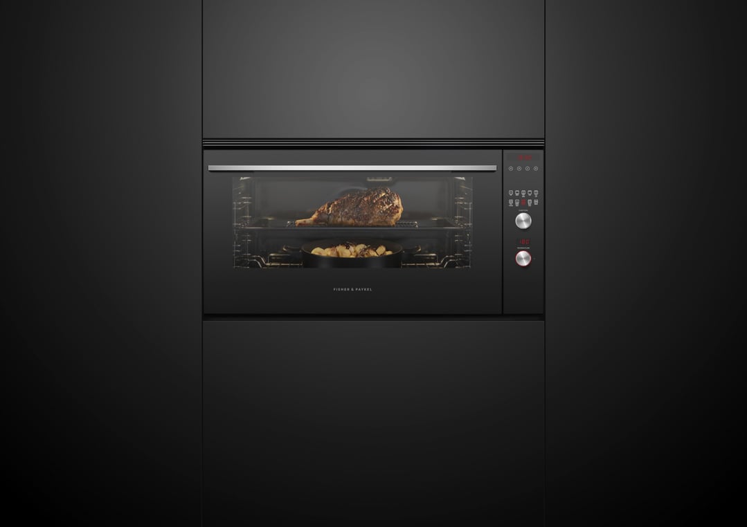 Black built-in oven cooking a roast and potatoes in a dark kitchen