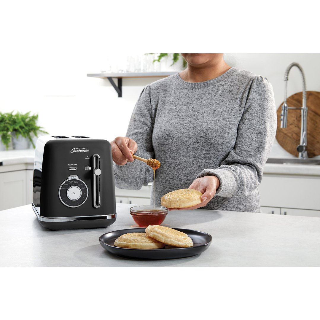 Woman drizzling honey onto toasted English muffins next to a black toaster