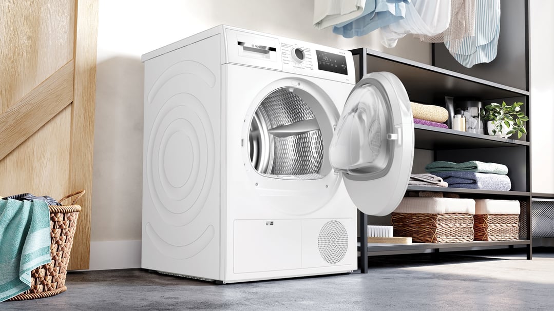 White Bosch heat pump tumble dryer with door open in a laundry room