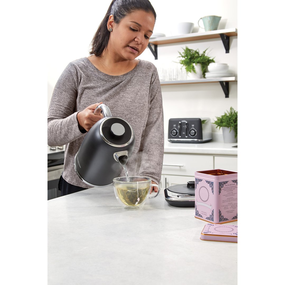 Woman pouring hot water from a black kettle into a glass teacup