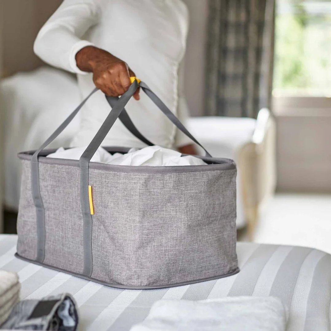 Person holding a grey Hold-All Collapsible Laundry Basket filled with white laundry