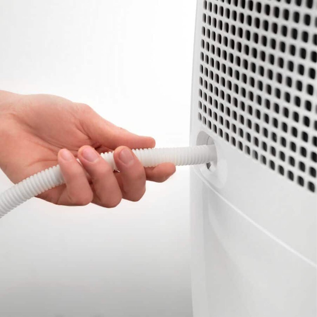 Hand inserting a white corrugated hose into the side of a dehumidifier