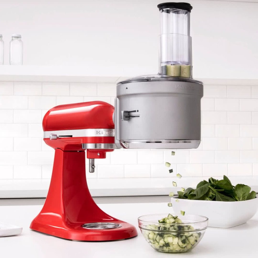 Red stand mixer with food processor attachment dicing vegetables into a glass bowl
