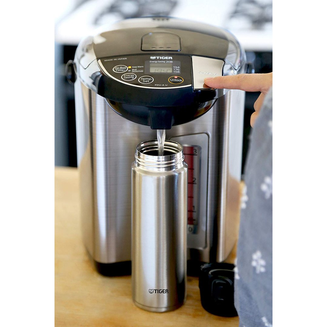 Hand pressing button on electric water heater to dispense water into a bottle