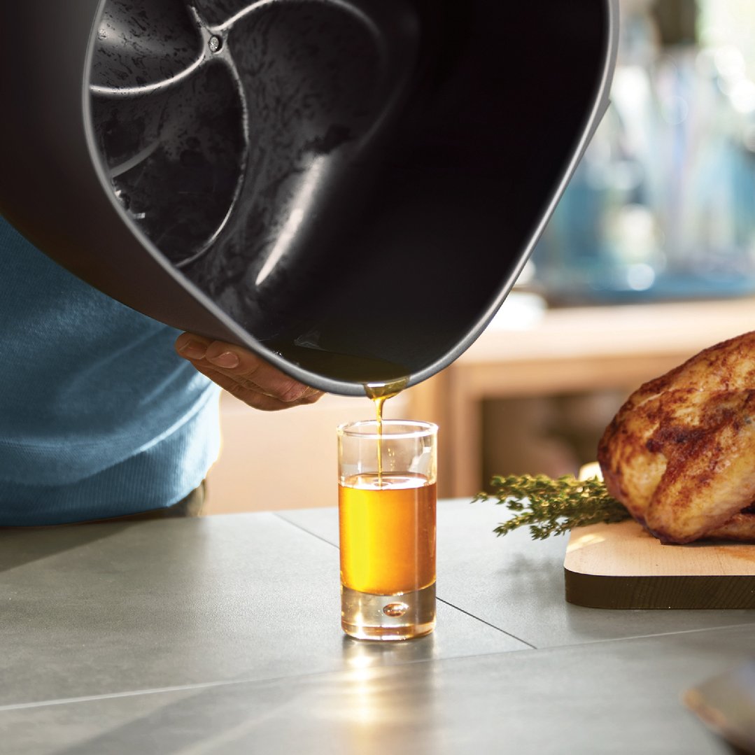 Hand pouring oil from an airfryer into a glass on a kitchen counter