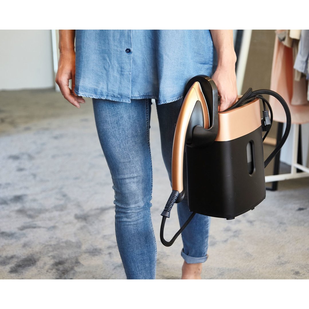 Person holding a black and copper garment steamer in a room