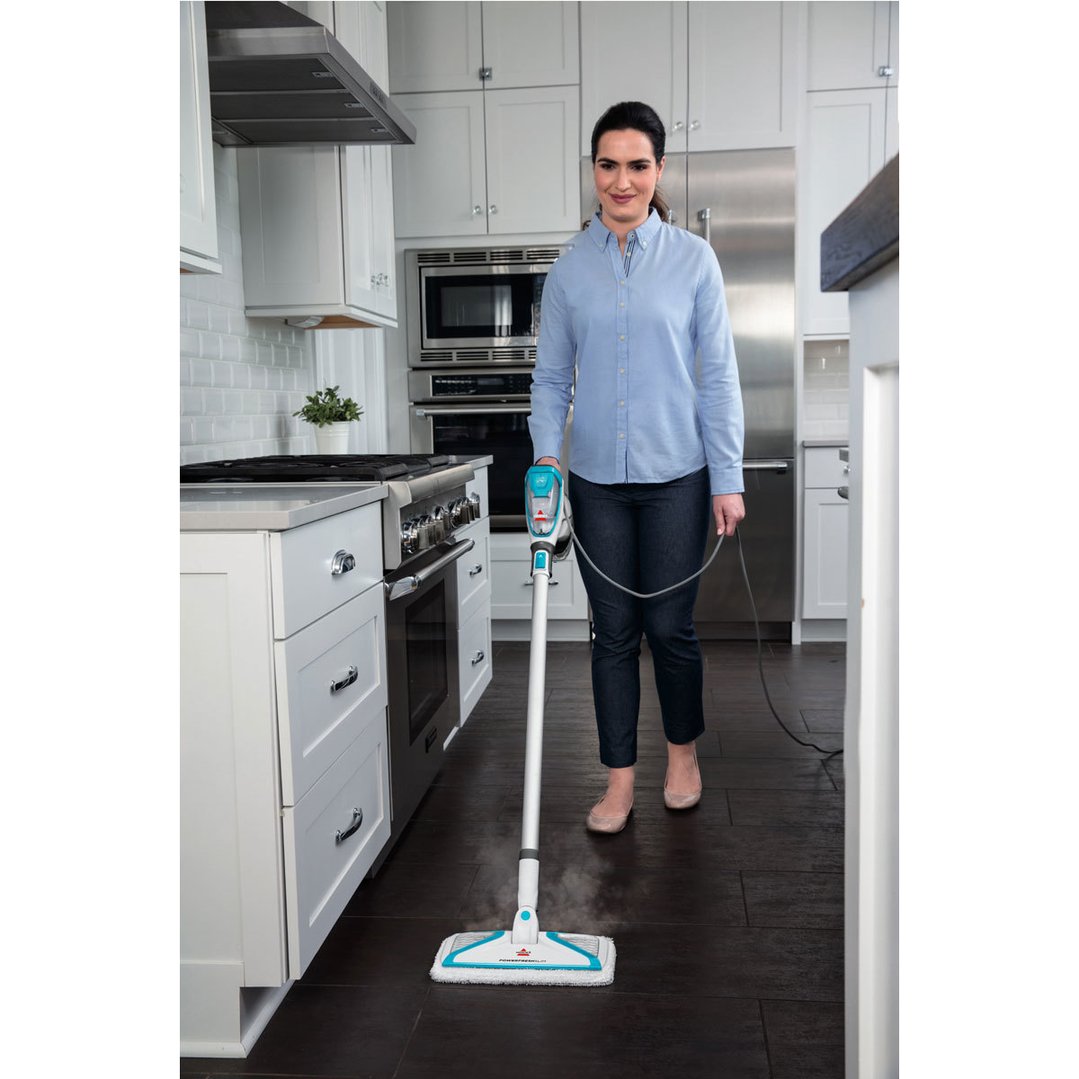 Woman steam mopping a dark floor in a white kitchen with a BISSELL steam mop