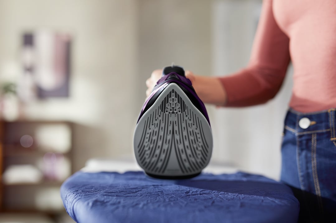 A person's hand holding a PHILIPS steam iron on an ironing board