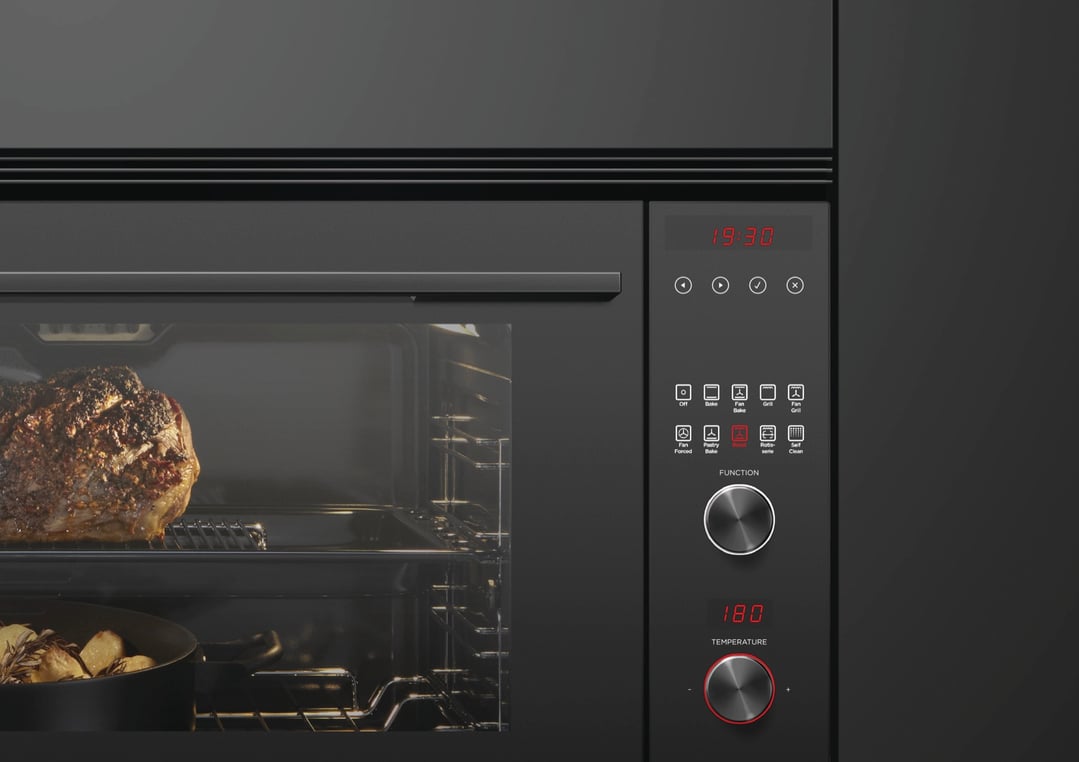 A built-in black oven with a roast and potatoes cooking inside