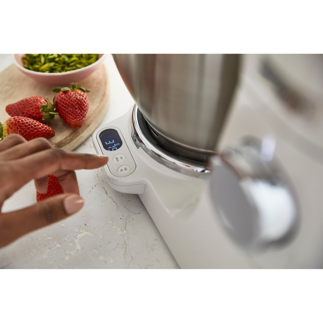 Hand pressing buttons on a white Kenwood food mixer with strawberries and pistachios