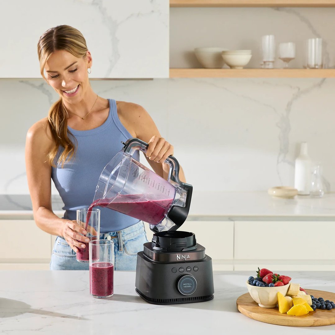 Woman pouring smoothie from Ninja blender into glasses on kitchen counter