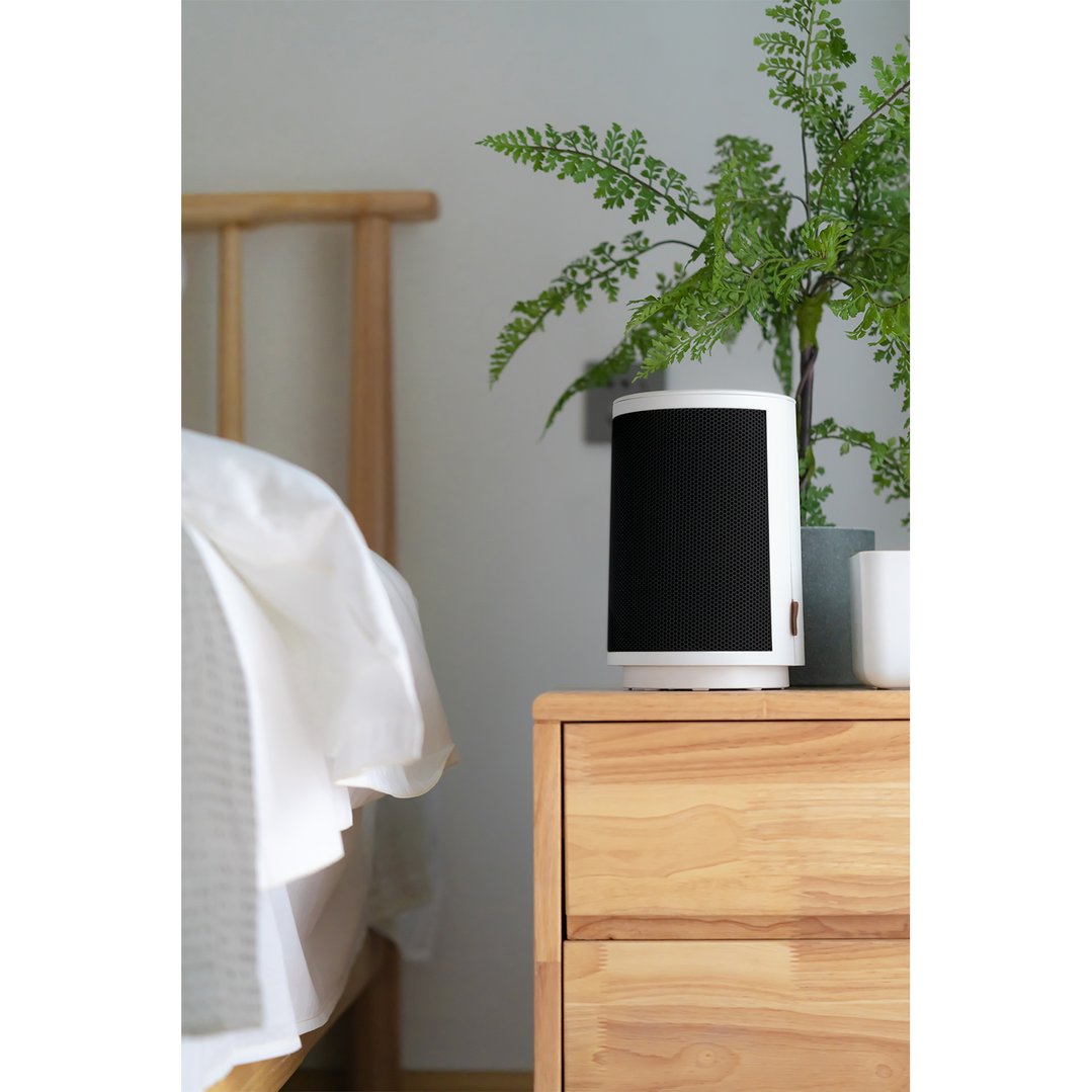 White ceramic heater on a wooden bedside table next to a bed