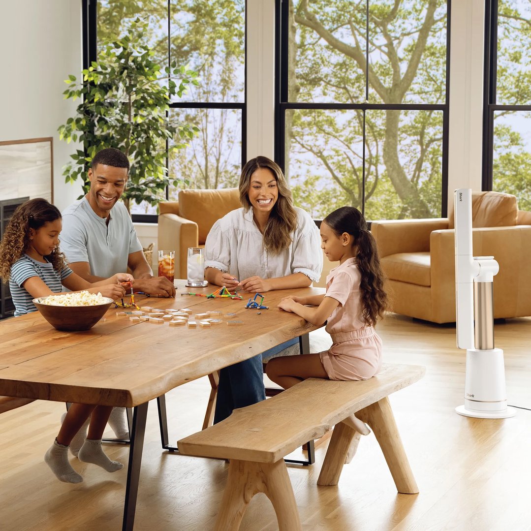 A family playing a board game at a wooden table with a fan nearby