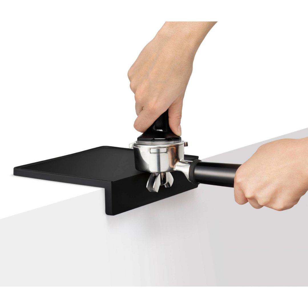 Hands tamping coffee grounds in a portafilter on a black coffee tamp mat