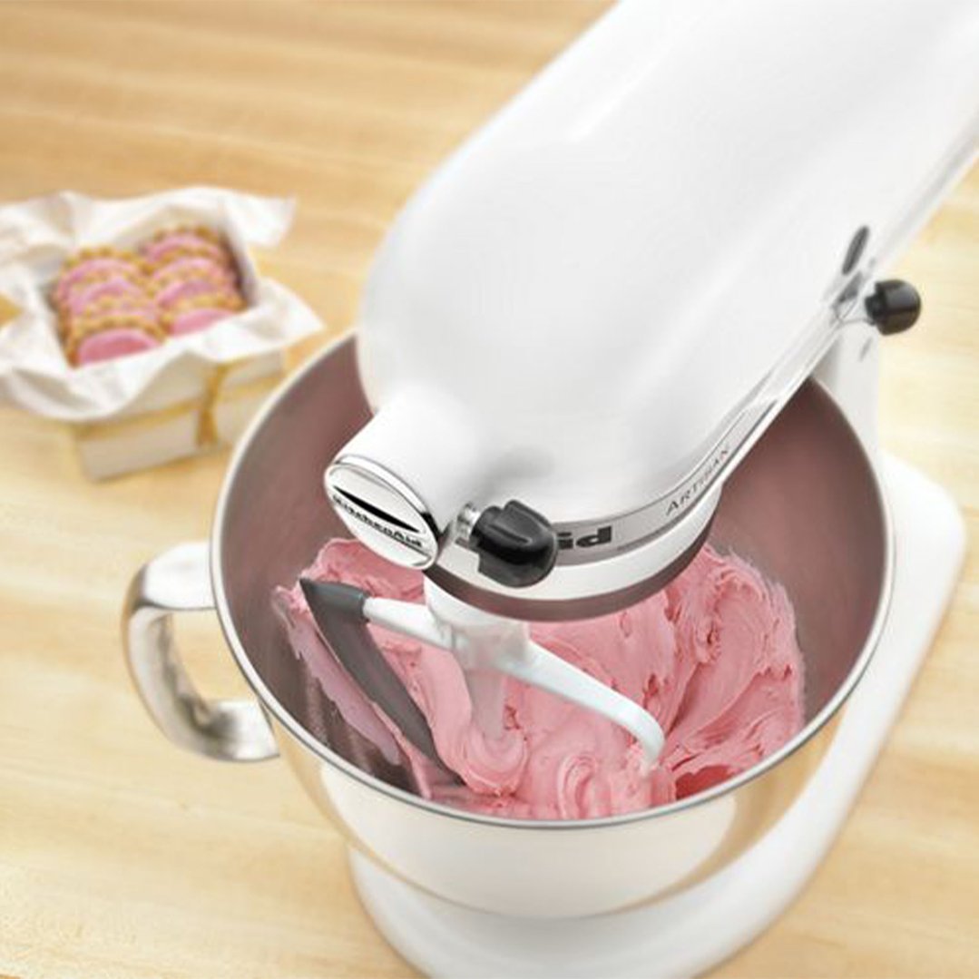 White stand mixer with pink frosting in bowl, cookies in background