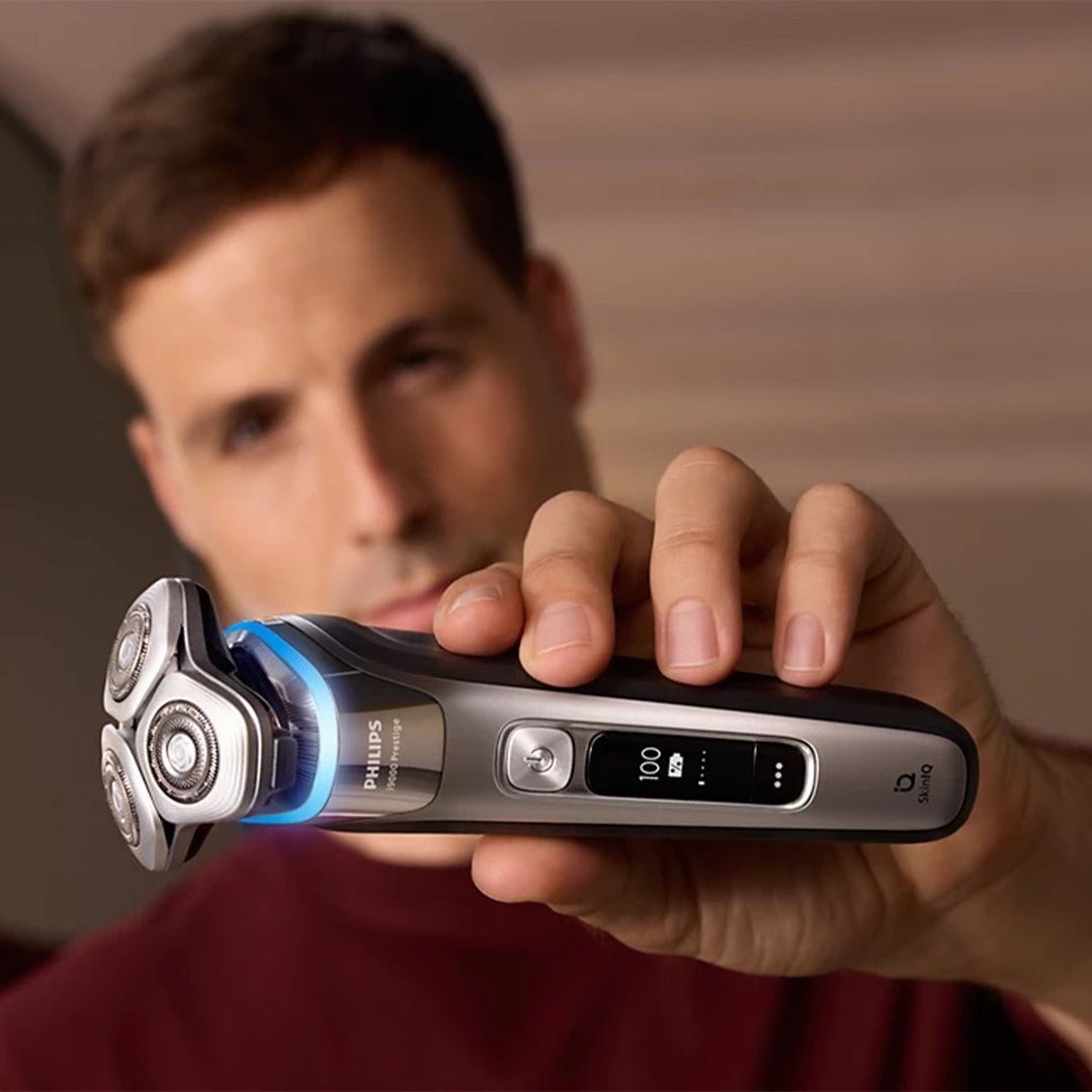 Man holding a Philips electric shaver with a blue light on its head
