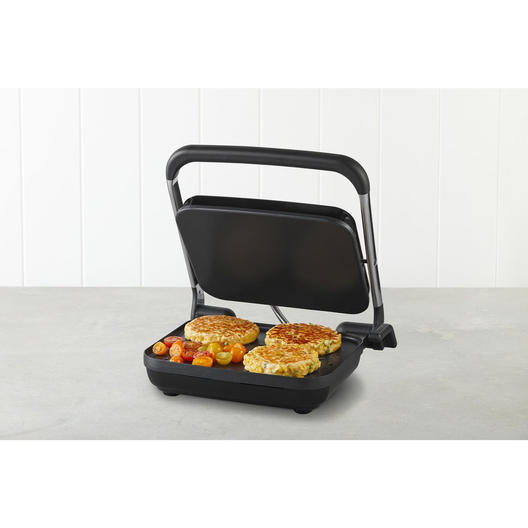 A sandwich press and grill cooking patties and tomatoes on a kitchen counter
