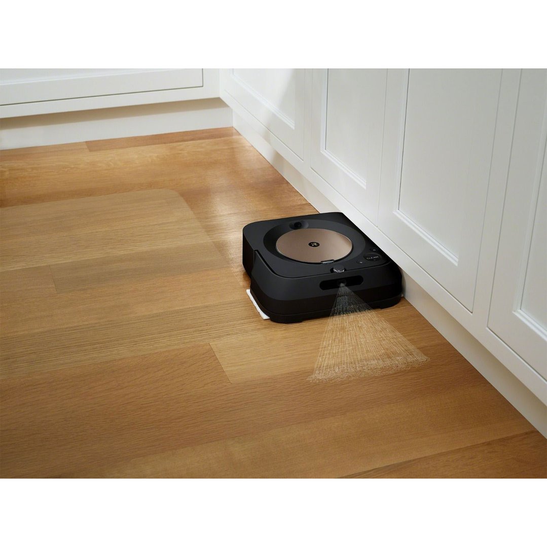 Black robot mop spraying water on a wooden floor next to white cabinets