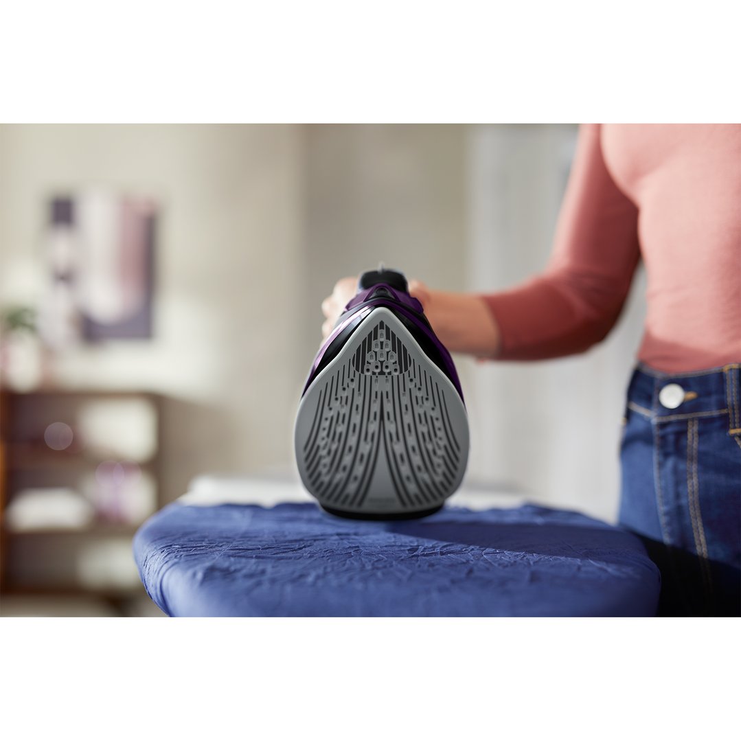 Person holding a purple steam iron on a blue ironing board
