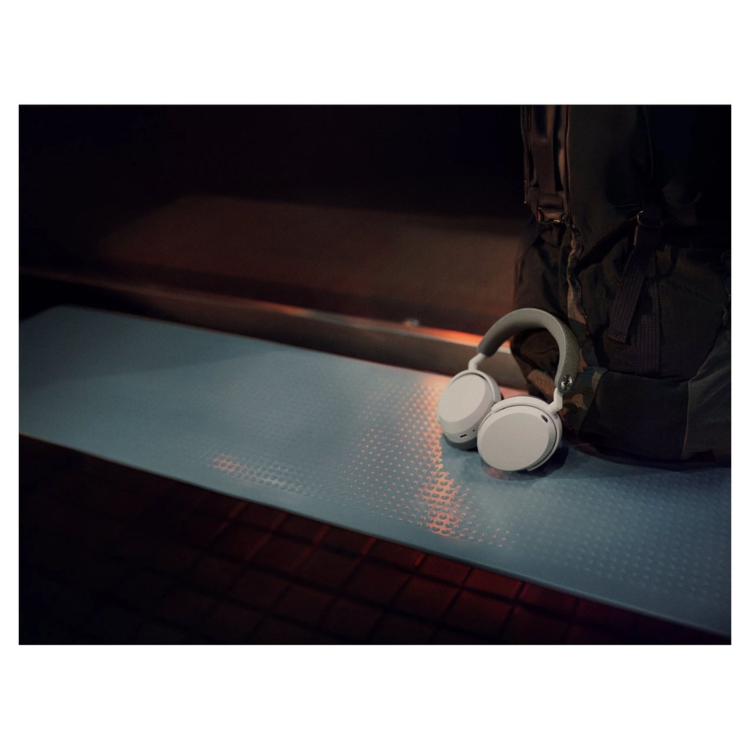 White wireless headphones resting on a blue surface next to a dark backpack
