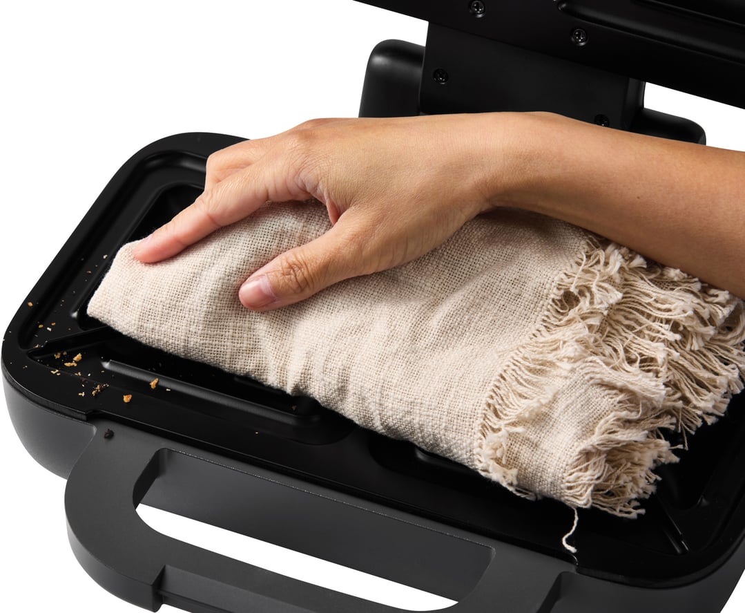 Hand wiping crumbs from the interior of a black 2 Slice Turbo Crunch Toastie Maker