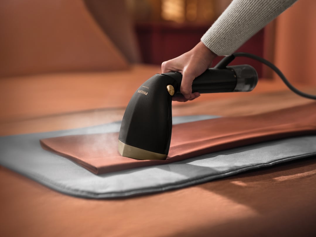Handheld garment steamer steaming a brown garment on a grey mat