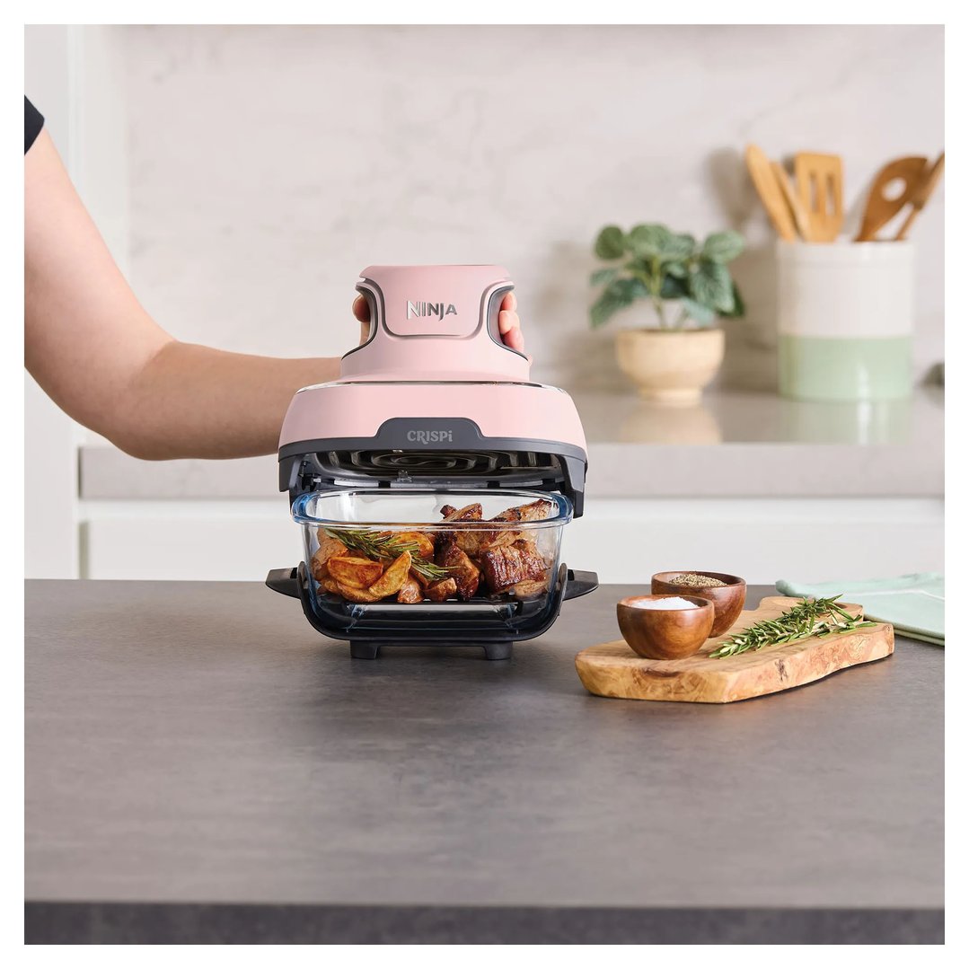 Person's hands holding a pink Ninja air fryer with food inside on a kitchen counter