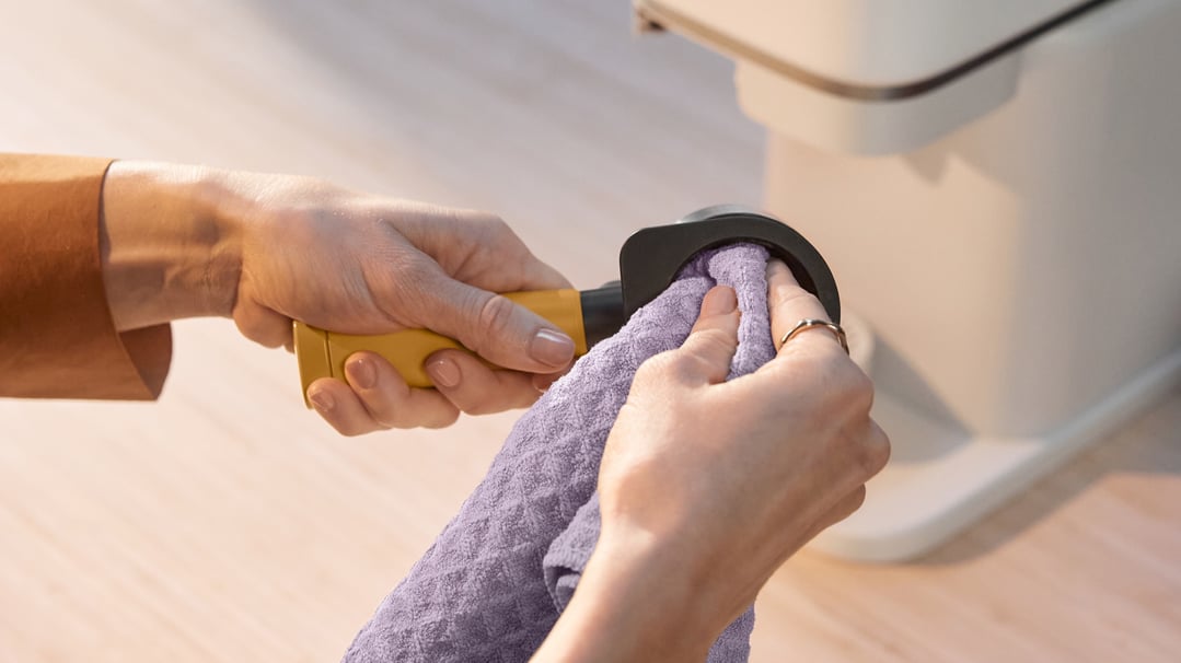 Hands cleaning a Baristina Portafilter with a purple cloth next to a coffee machine