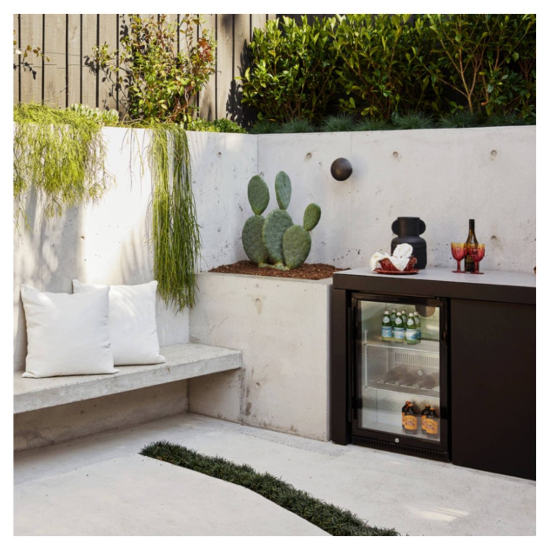 Outdoor beverage chiller integrated into a concrete and plant-filled patio setting