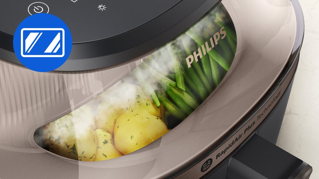 Close-up of a Philips airfryer with potatoes and green beans steaming inside