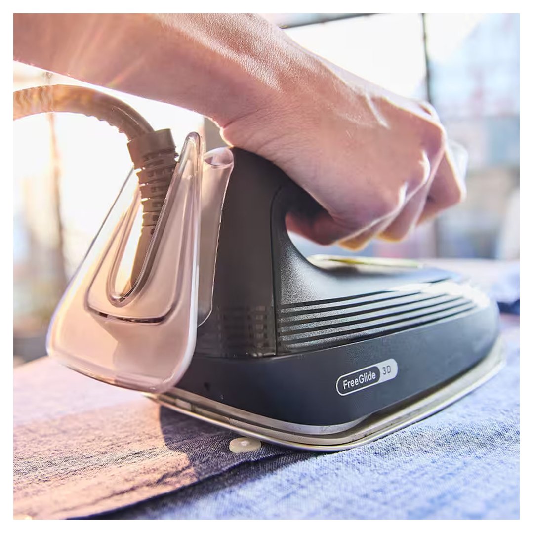 Hand holding a Braun CareStyle 3 steam generator iron on a blue shirt