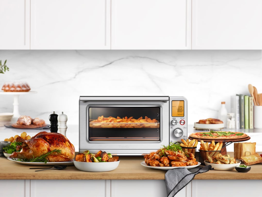 Breville Smart Oven Air Fryer XL on a kitchen counter surrounded by food
