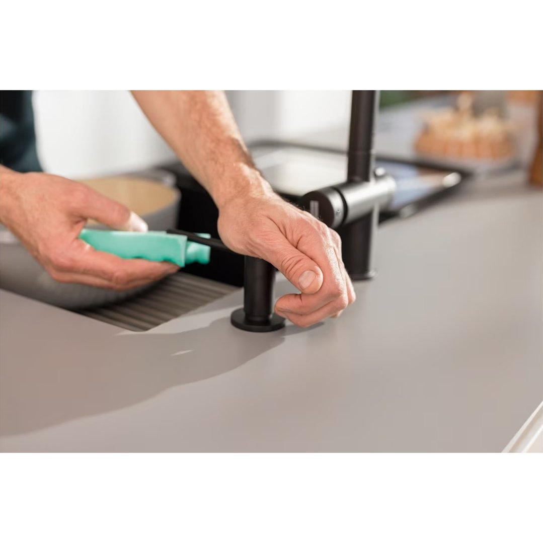 Person's hands installing a black soap dispenser into a kitchen counter