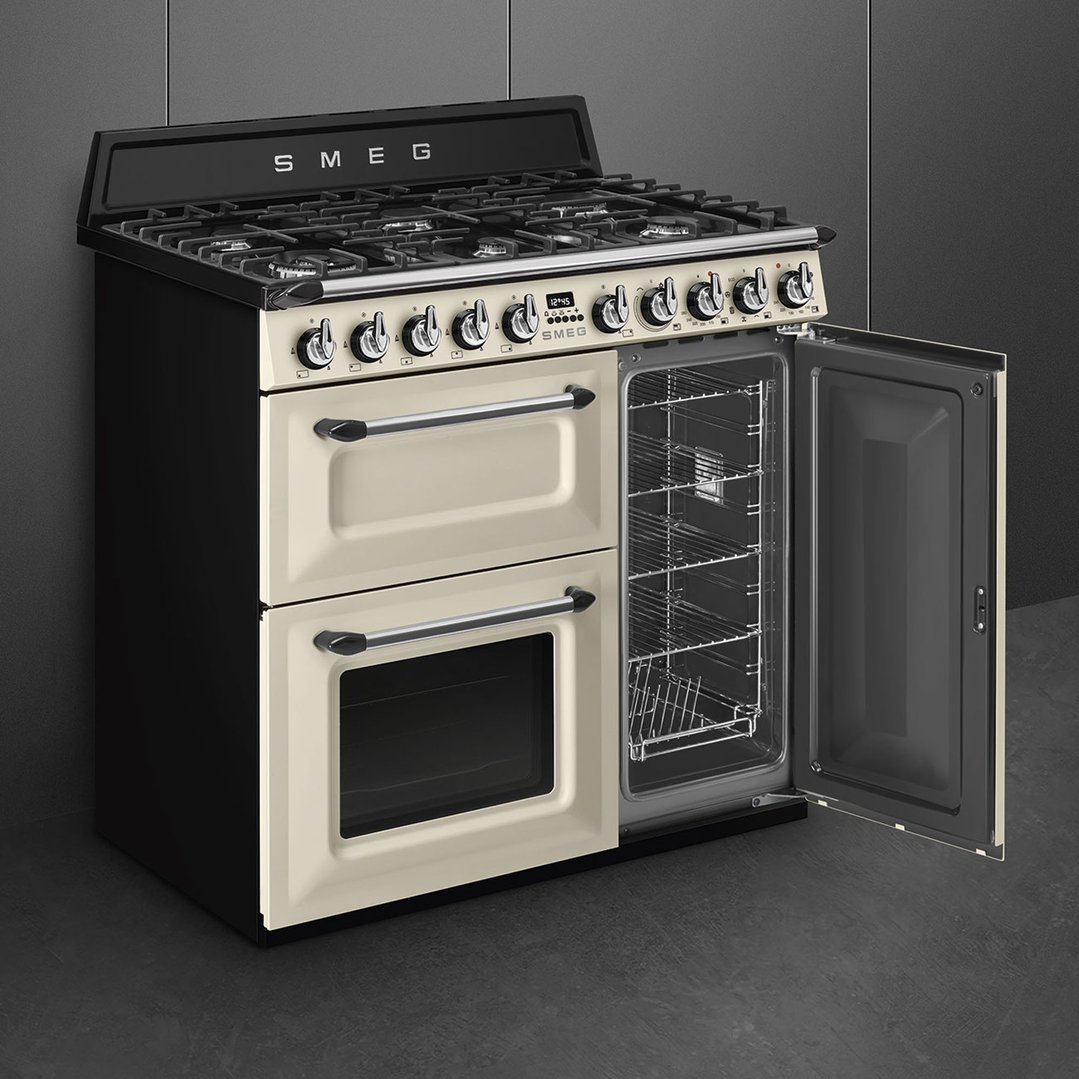 A cream SMEG freestanding cooker with an open oven door in a dark kitchen