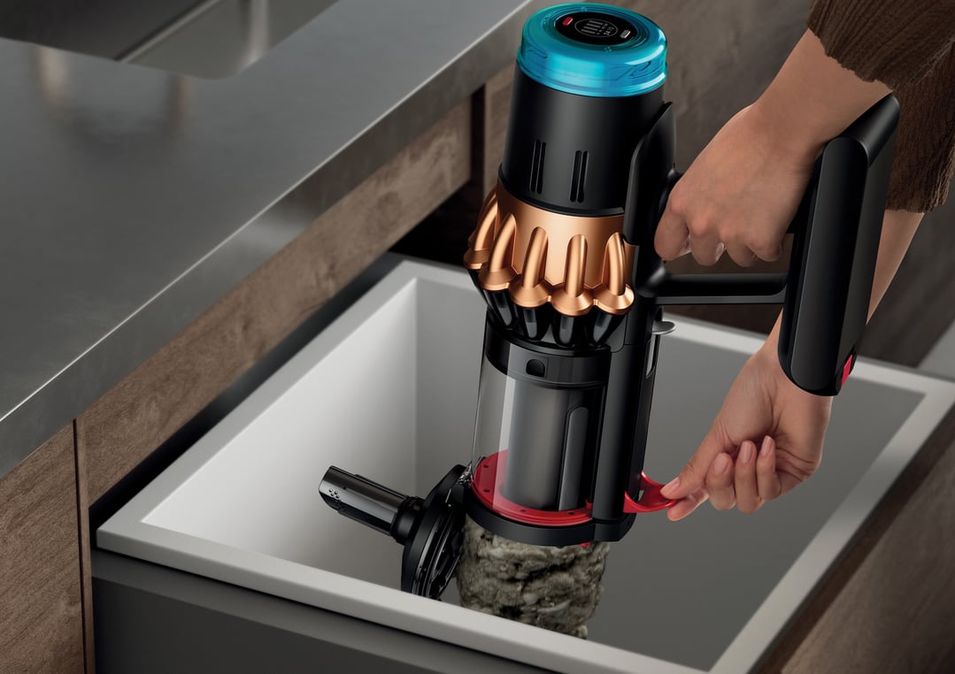 Hands emptying a Dyson handStickVacuum into a sink, showing collected debris